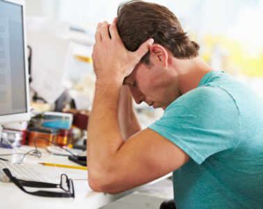 Stressed Man Working At Desk In Busy Creative Office