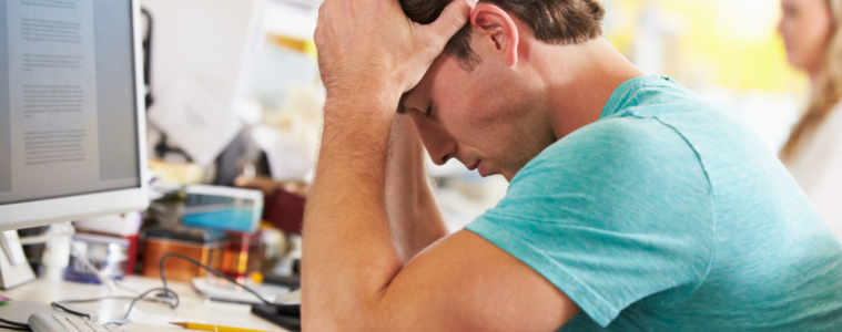 Stressed Man Working At Desk In Busy Creative Office