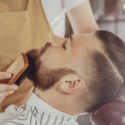 The Barber Combs The Man's Beard With A Brush. Photo In Vintage Style
