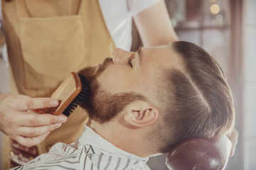 The Barber Combs The Man's Beard With A Brush. Photo In Vintage Style