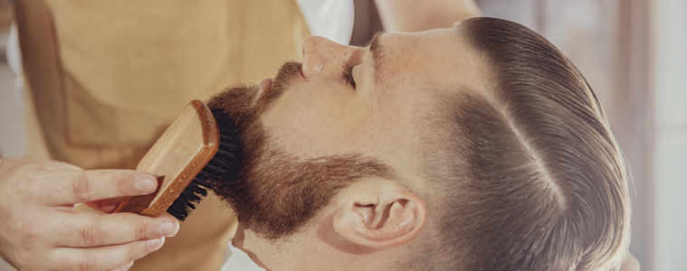 The Barber Combs The Man's Beard With A Brush. Photo In Vintage Style